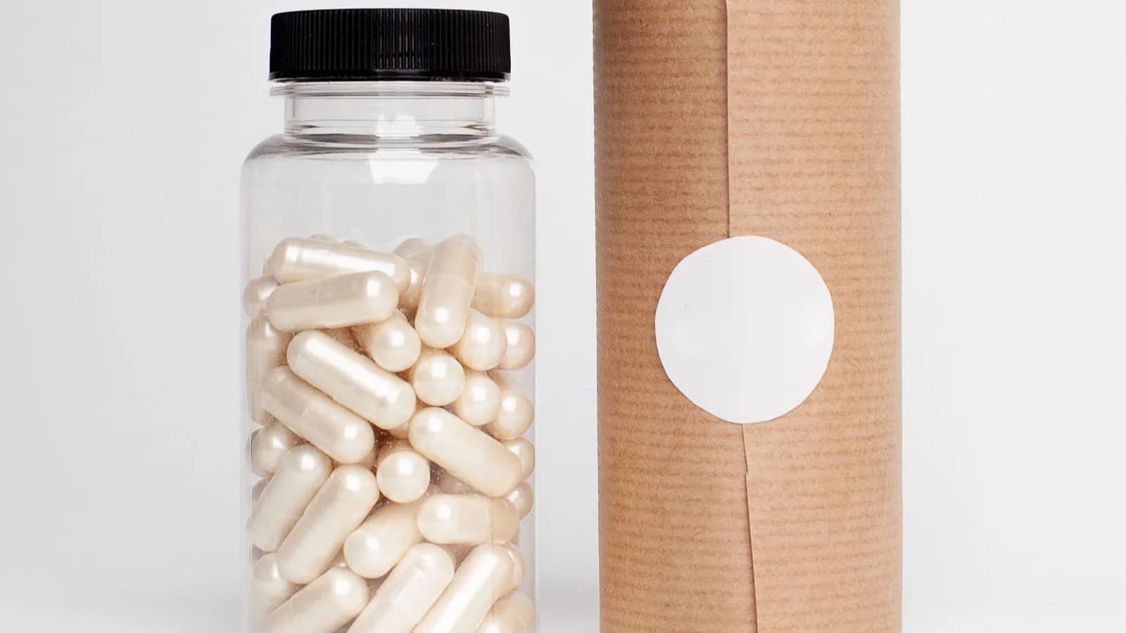 Clear bottle of white capsules beside unbranded kraft packaging